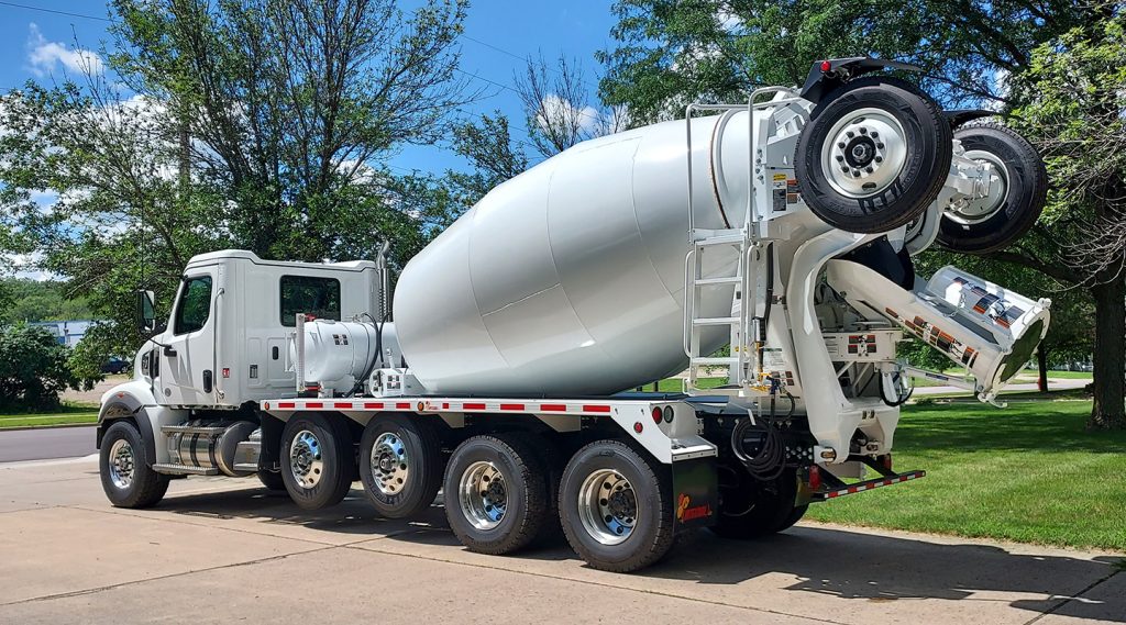 The left rear side of an INTEGRALdx concrete redi-mix truck colored in white. It has a booster axle attached in the back.