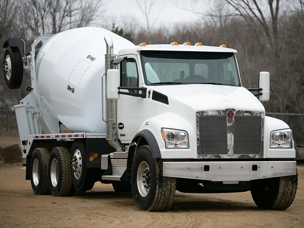 A white INTEGRAldx concrete ready-mix truck with a Kenworth chassis and booster axle.