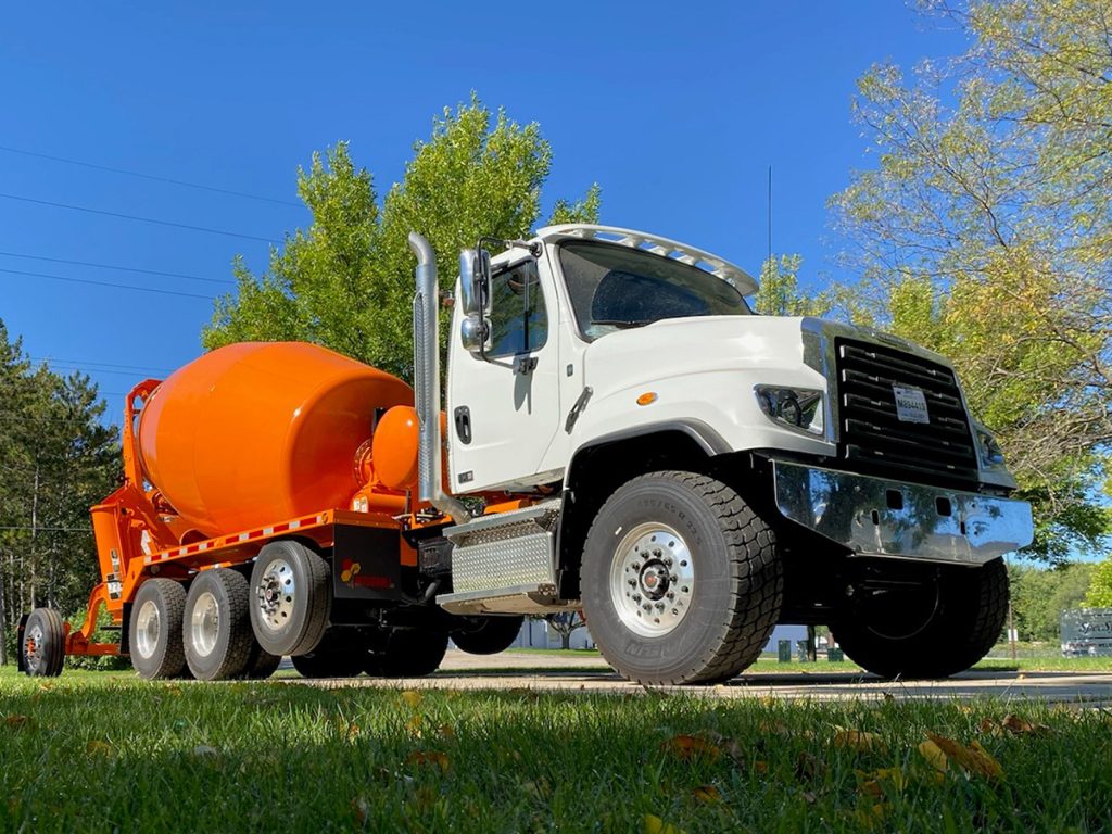 An INTEGRALdx concrete ready mix truck. It has a white Western Star chassis with an orange rear section. It is a conventional.