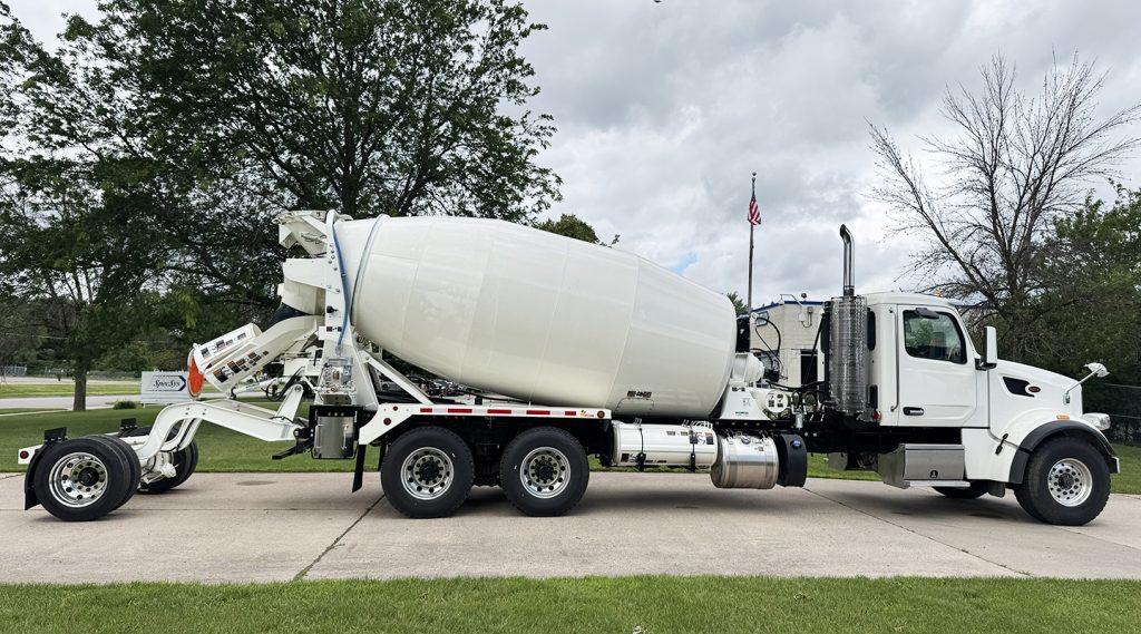 The right side of a 14 cubic yard INTEGRALdx concrete redi-mix truck with a booster axle lowered to the ground. It is colored white.