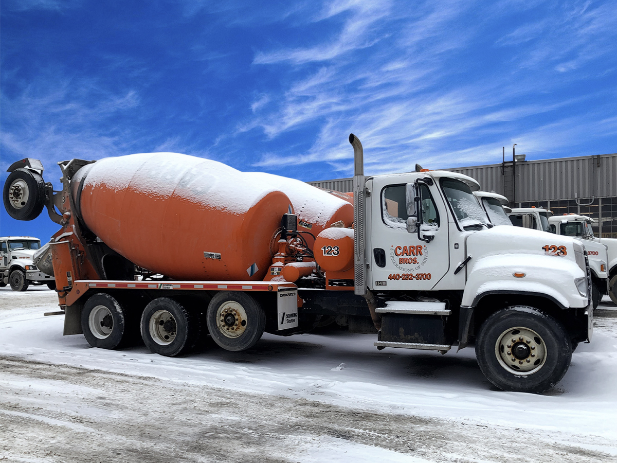 The right side of an INTEGRALdx concrete redi-mix truck made for Carr Bros. It has a booster axle, an orange drum, and a Carr Bros. logo on the passenger-side door.