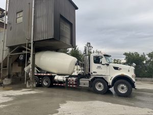 The passenger-side view of an INTEGRALdx concrete redi-mix booster truck with a drum fill line of 14 cubic yards of concrete. The passenger-side door of the Peterbilt chassis has a decal for M&K Ready Mix Inc.