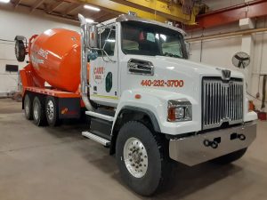 The front right view of an INTEGRALdx concrete redi-mix booster truck made for Carr Bros, which includes a white front Western Star chassis and an orange mixer body. Both the front and rear feature Carr Bros. decals.