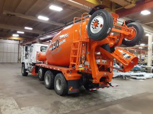 The rear left view of an INTEGRALdx concrete redi-mix booster truck made for Carr Bros, which includes a white front Western Star chassis and an orange mixer body. Both the front and rear feature Carr Bros. decals. The booster tag axle in the back is fully raisd up.