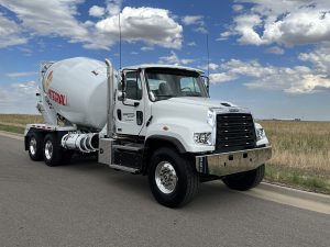 The front right side of a conventional-styled INTEGRALdx concrete redi-mix truck built for TransCHICAGO, who represented us at the National Ready Mixed Concrete Association's annual tournament. An INTEGRALdx logo is visible along the drum. It has a Freightliner chassis.