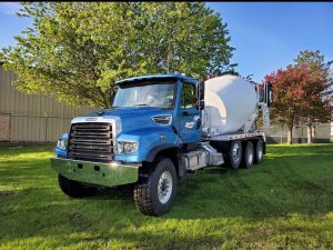 The front left side of a blue INTEGRALdx concrete redi-mix truck with a booster axle, which was built for Schwartz Excavating & Redi-Mix. An INTEGRALdx logo is visible along the drum. It has a Freightliner chassis.