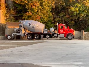 The right side view of an INTEGRALdx concrete redi-mix booster truck at a worksite. This truck has a red Peterbilt chassis and a gray drum with Stamm's logo, all caps with the S being encased inside a badge. There is also a logo on the passenger-side door.