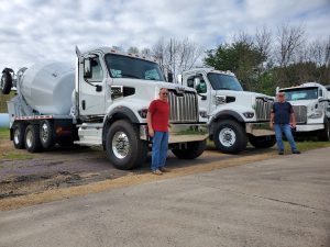 Two men standing in front of their three INTEGRALdx concrete redi-mix trucks. All three are white Western Stars with booster tag axles.