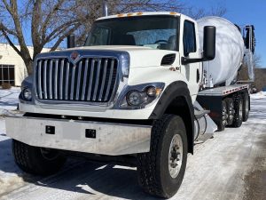 A front left close-up view of an INTEGRALdx concrete redi-mix booster truck, which has a completely white mixer body. Its chassis brand is International.