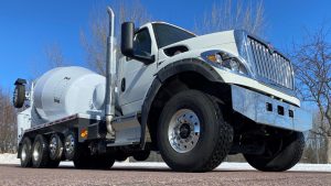 A front lower right close-up view of an INTEGRALdx concrete redi-mix booster truck, which has a completely white mixer body. Its chassis brand is International.