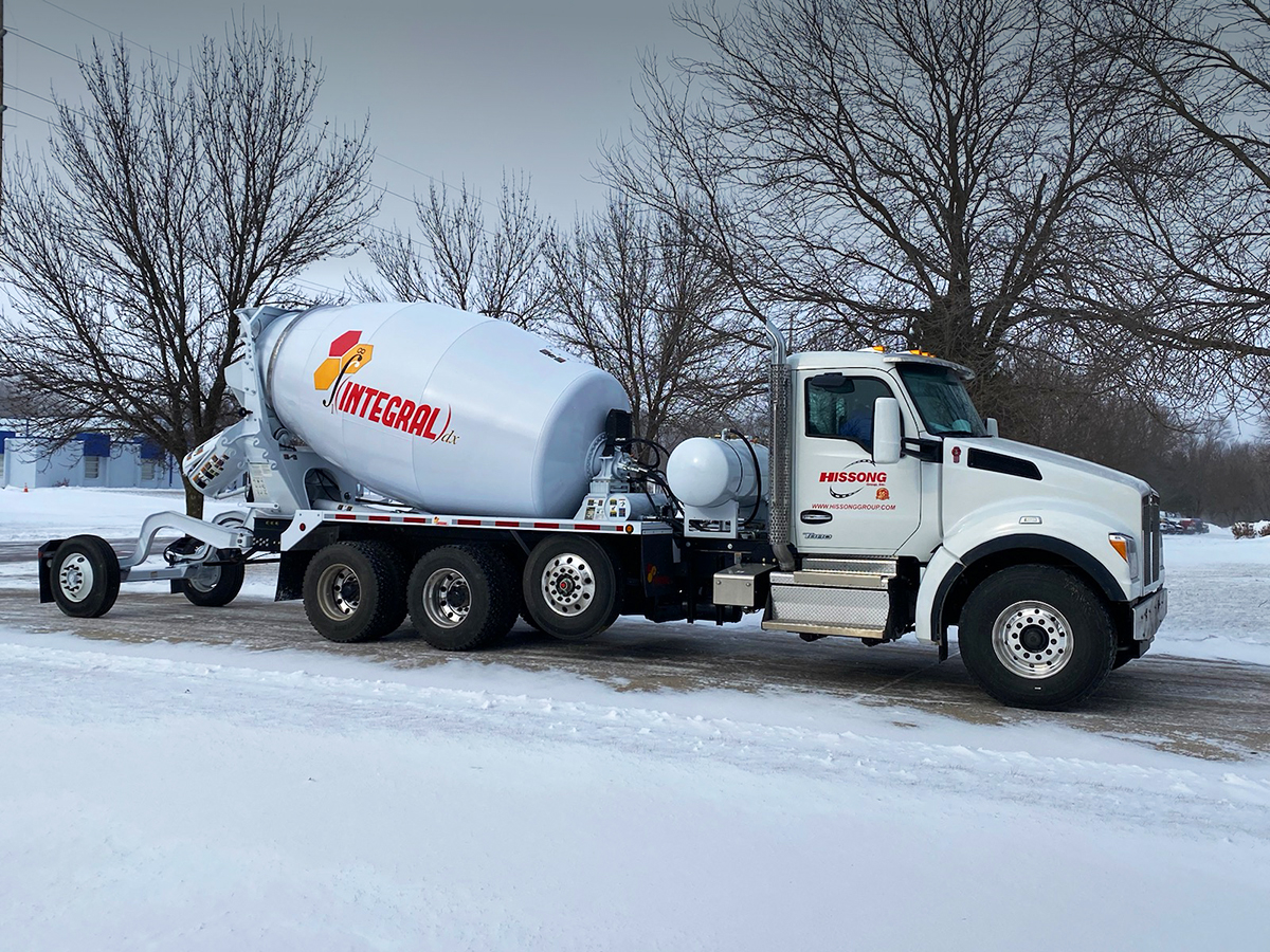 The right side view of an INTEGRALdx concrete redi-mix truck with its booster axle lowered down to the ground. This truck features a Kenworth chassis with a Hissong logo on the passenger-side door.