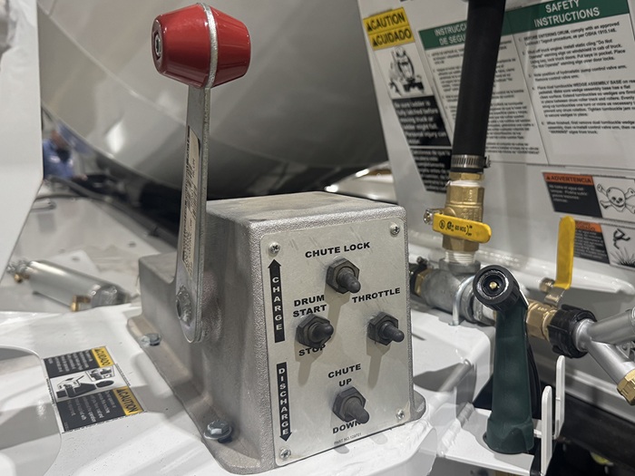A view of an INTEGRALdx concrete redi-mix truck's rear cable controls, featuring a red and gray lever and four toggle switches for locking the chute, starting or stopping the drum, throttling, and moving the chute up or down.