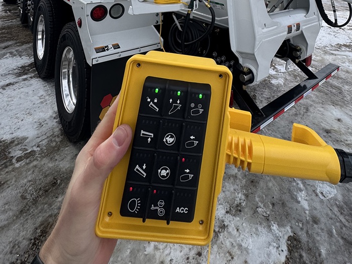 A rear pendant controller for an INTEGRALdx concrete redi-mix truck. The yellow, cable-attached pendant has a total of 12 buttons. In this image, it is being held in someone's hand.